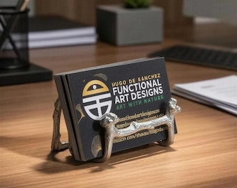 May include: A silver-toned metal business card holder featuring a textured, branch-like design. It holds a stack of black business cards with the text "HUGO DE SANCHEZ FUNCTIONAL ART DESIGNS ART WITH NATURE" printed in white, gold, and green.