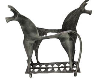 May include: A dark gray metal sculpture featuring two stylized, elongated horse figures standing on a rectangular base with a cut-out diamond pattern. The horses have open mouths, slender bodies, and long tails, with a textured, matte finish throughout.