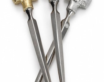 May include: Three metal letter openers with handles shaped like stylized human faces. One handle is gold-toned, while the other two are silver-toned. Each face features a small blue gemstone set into the forehead and a pointed, smooth blade.