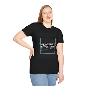 May include: Black t-shirt with a square graphic featuring the text "STAY CURIOUS" and a colorful illustration of two hands almost touching. The shirt is worn by a person in blue jeans.