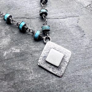 May include: Silver-toned necklace featuring turquoise-colored beads and a textured, square pendant with a smaller square inset. The necklace has a delicate chain and a handcrafted appearance, suitable for everyday wear.