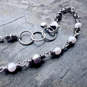 May include: A silver necklace with a chain and clasp. The necklace features white pearl beads and a hammered silver bead. The chain is made of small, twisted silver links.