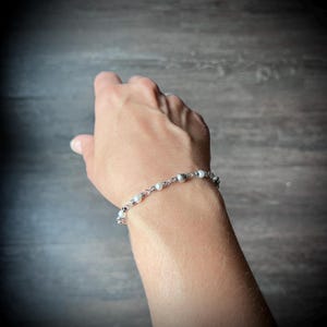 May include: A delicate silver bracelet featuring small, round, white pearls and silver beads. The bracelet is strung on a fine chain and is displayed on a person's wrist.