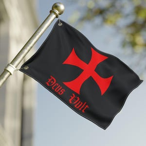 Könnte beinhalten: Eine schwarze Flagge mit einem großen roten Kreuz und dem Schriftzug "Deus Vult" in roter Schrift. Die Flagge ist an einer goldenen Stange befestigt und weht im Wind vor blauem Himmel.