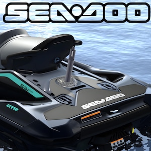 Puede incluir: Una moto de agua Sea-Doo GTR en gris oscuro con detalles en color cerceta, con una etiqueta de motor Rotax, una cubierta trasera con el logotipo de Sea-Doo y un soporte de cámara vertical instalado en la plataforma trasera, sobre agua azul.