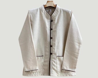 May include: A beige jacket with a mandarin collar, dark brown trim, and button closures. The jacket has two front pockets and long sleeves. The garment is hanging on a wooden hanger.