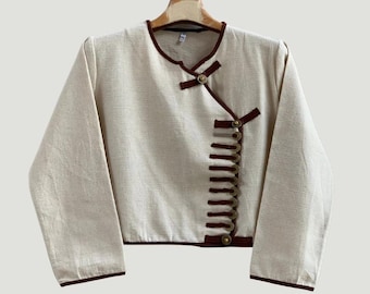 May include: A cream-colored, long-sleeved shirt with a brown trim and a row of gold buttons down the side.