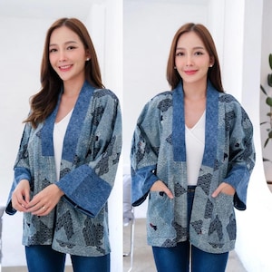Puede incluir: Chaqueta estilo kimono azul y gris estampada, con cuello y puños en contraste tipo denim. La chaqueta presenta un diseño de olas y pájaros, con dos bolsillos delanteros. La modelo lleva un top blanco y vaqueros azules.