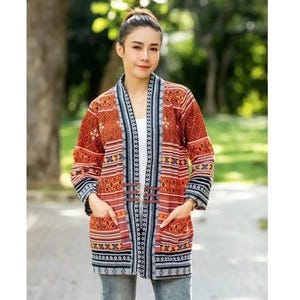 Puede incluir: Chaqueta larga y abierta con un vibrante estampado geométrico en tonos naranja, rojo, negro y blanco. La chaqueta presenta mangas largas, bolsillos y un cierre decorativo. La chaqueta se lleva sobre una camiseta blanca y vaqueros azules.