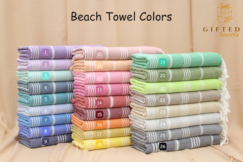May include: Stacks of colorful beach towels in various shades, including purple, pink, green, and blue. Each towel has white stripes and a fringed edge. The text "Beach Towel Colors" is at the top.