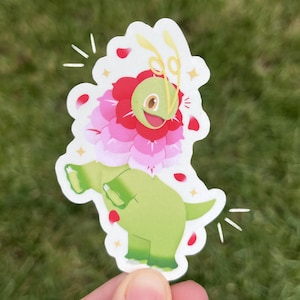 May include: A die-cut sticker featuring a green dinosaur with a flower-like head and a smiling face. The flower is pink and red with yellow accents. The sticker is held against a green grassy background.