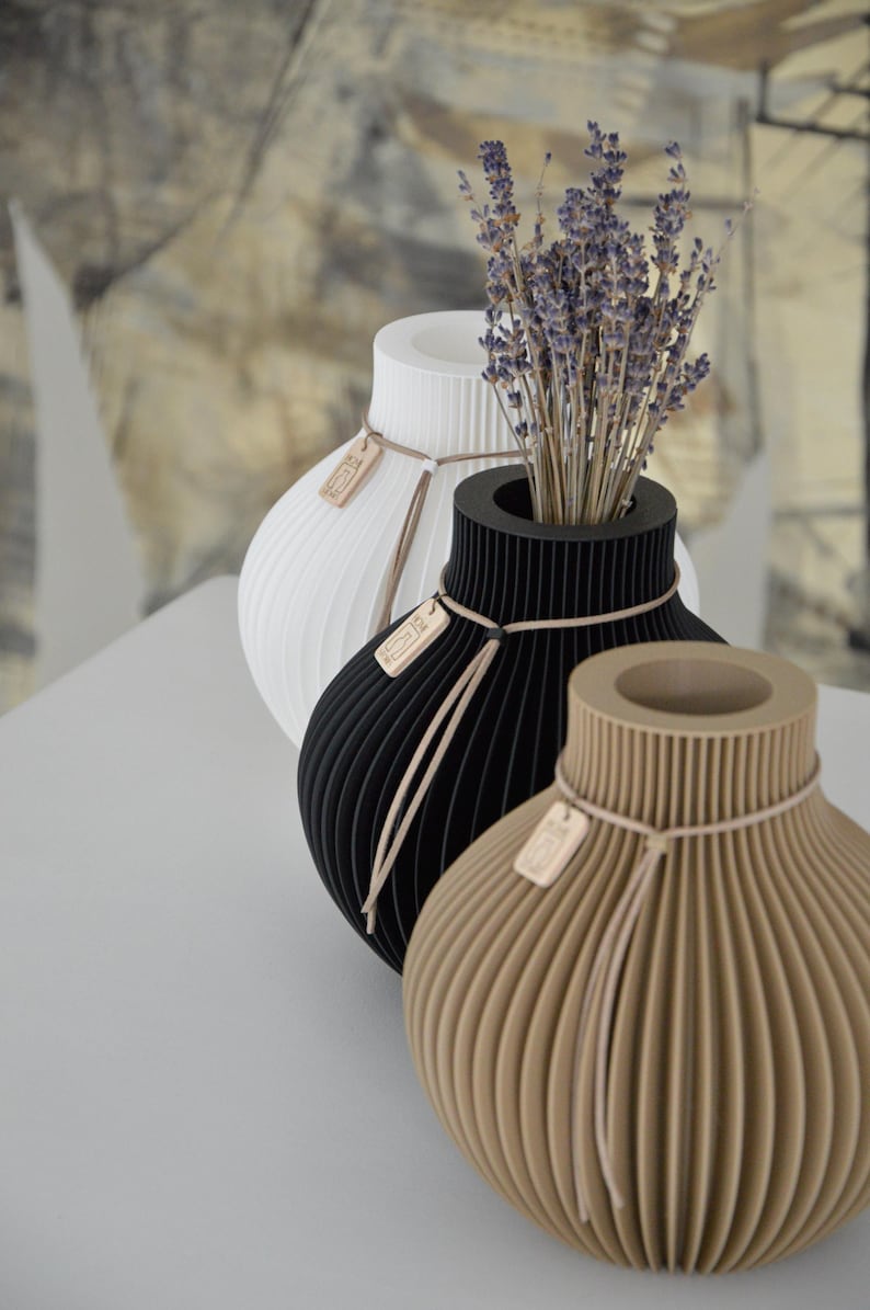 May include: Three decorative vases in white, black, and tan, each with a unique ribbed design. The black vase holds dried lavender. Each vase has a small wooden tag tied with twine. The vases are approximately 8 inches tall.