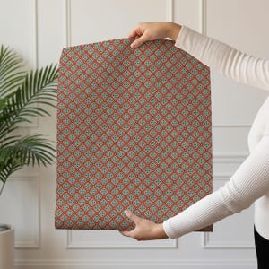 May include: A rectangular sheet of wrapping paper featuring a repeating geometric pattern of orange diamond shapes outlined in dark lines, each containing a small central floral motif in shades of teal, white, and yellow against a light background.