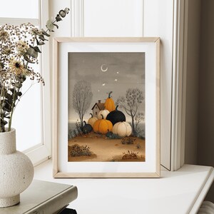 May include: Framed art print depicting a harvest scene with pumpkins. The artwork shows a small house, trees, and pumpkins in shades of orange, black, and white. The sky is a muted grey with a crescent moon and stars, creating a seasonal atmosphere.