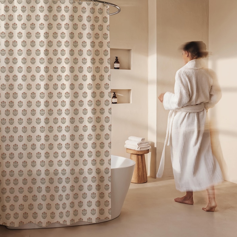 May include: A beige shower curtain with a repeating floral pattern in muted red and green. The curtain hangs from a curved metal rod. The bathroom has a white tub, wooden stool, and a person wearing a white robe.