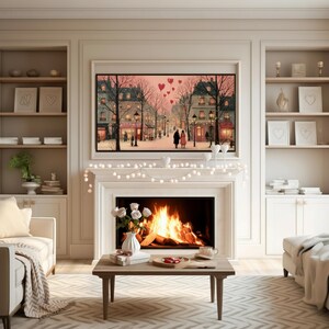 May include: A cozy living room scene with a fireplace, artwork, and decorative elements. A framed painting depicts a romantic street scene with a couple. A coffee table holds a vase of white roses, gifts, and a tray of treats. A string of lights adorns the mantel.