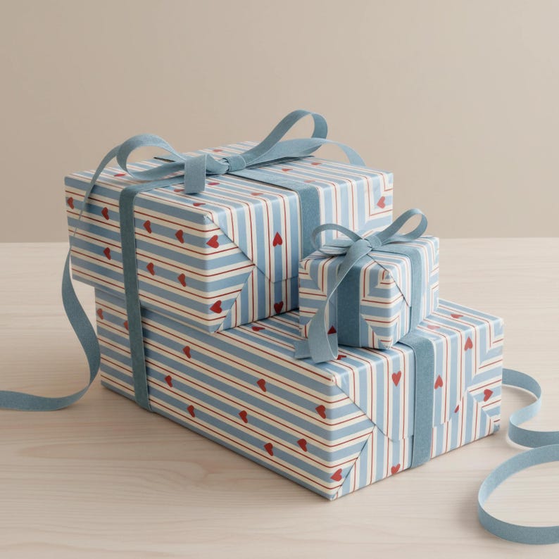 May include: Three wrapped gift boxes stacked on top of each other. The boxes are wrapped in light blue paper with red hearts and vertical stripes. Each box is tied with a light blue ribbon.