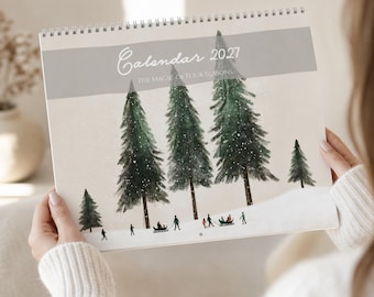 May include: A 2027 wall calendar with a spiral binding at the top. The cover features a watercolor illustration of dark green pine trees in a snowy landscape with small figures sledding. The text reads Calendar 2027 The Magic of Four Seasons.