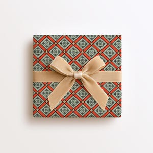 May include: A square gift box wrapped in paper featuring a repeating diamond pattern in orange and muted green, with each diamond containing a small floral motif. A wide, smooth, beige velvet ribbon is tied in a bow across the centre.