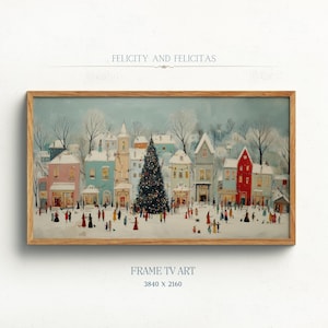 May include: A framed print of a winter village scene with a large Christmas tree in the center. The artwork features colorful buildings, snow-covered rooftops, and figures of people. The text "FELICITY AND FELICITAS" is at the top.