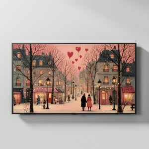 May include: A framed print of a romantic winter scene. The artwork depicts a snowy street with buildings, streetlights, and a couple walking. Red heart-shaped balloons float in the pink sky. The overall color palette is soft with pinks, reds, and whites.
