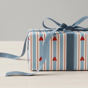 May include: A wrapped gift box with a blue ribbon. The gift wrap features a pattern of red hearts and vertical stripes in blue and white. The blue ribbon is tied in a bow.
