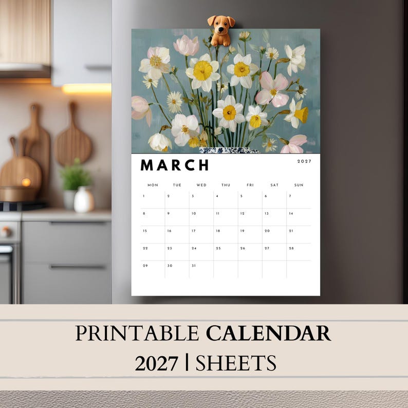 May include: A 2027 wall calendar for the month of March featuring a floral illustration of white and yellow daffodils in a blue and white patterned vase, topped with a small brown dog magnet on a gray refrigerator surface.