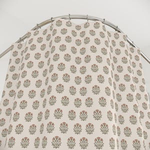 May include: A shower curtain with a repeating floral pattern. The flowers are a muted red-orange color with green leaves, set against a cream-colored background. The curtain hangs from a curved, silver-colored shower rod.