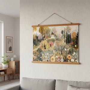 May include: A landscape art print featuring a whimsical scene of a small white house nestled among colorful trees and flowers. The artwork is displayed on a wooden frame and suspended by a natural rope, adding a touch of rustic charm to the wall decor.