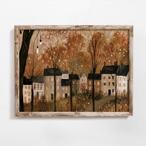 Peut inclure: Une impression d'art encadrée représentant une rangée de maisons nichées parmi des arbres d'automne avec des guirlandes lumineuses chaudes suspendues aux branches. La scène présente une palette de tons bruns, orange et crème.