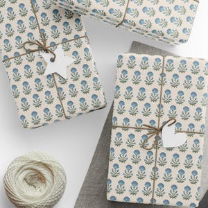 May include: Several wrapped gifts with floral patterned paper in cream and blue. The gifts are tied with twine and have white paper tags. A ball of twine and a gray cloth are also visible.