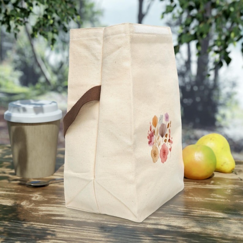 A Reusable Cotton Lunch Tote with strap decorated with a watercolor floral pattern, perfect as a picnic accessory or travel lunch bag.