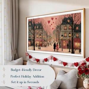 May include: A framed art print depicts a romantic winter scene of a European street with couples, buildings, and heart-shaped balloons. The print is in a gold frame, with a red and pink heart garland below. Text on the image reads: Budget-friendly Decor, Perfect Holiday Addition, Set it up in Seconds.