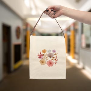 This Cute Watercolor Floral Lunch Bag is made from durable cotton canvas with a strap and loop tape closure, ideal for children or adults.