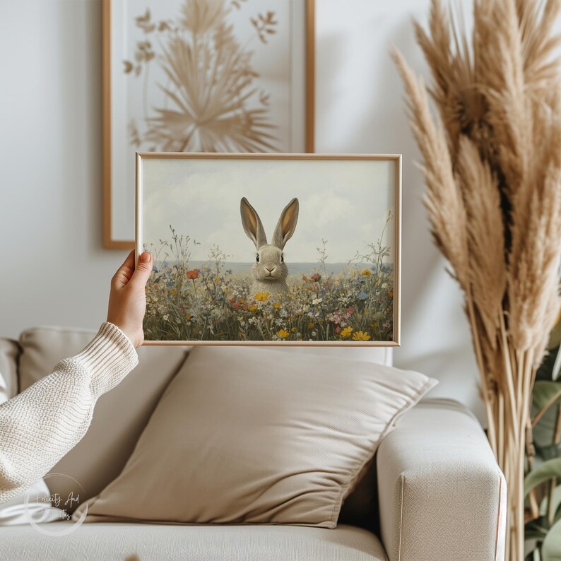K&ouml;nnte beinhalten: Ein gerahmter Druck eines wei&szlig;en Kaninchens, das in einem Feld voller Wildblumen sitzt. Das Kaninchen schaut den Betrachter direkt an, die Ohren aufgestellt.
