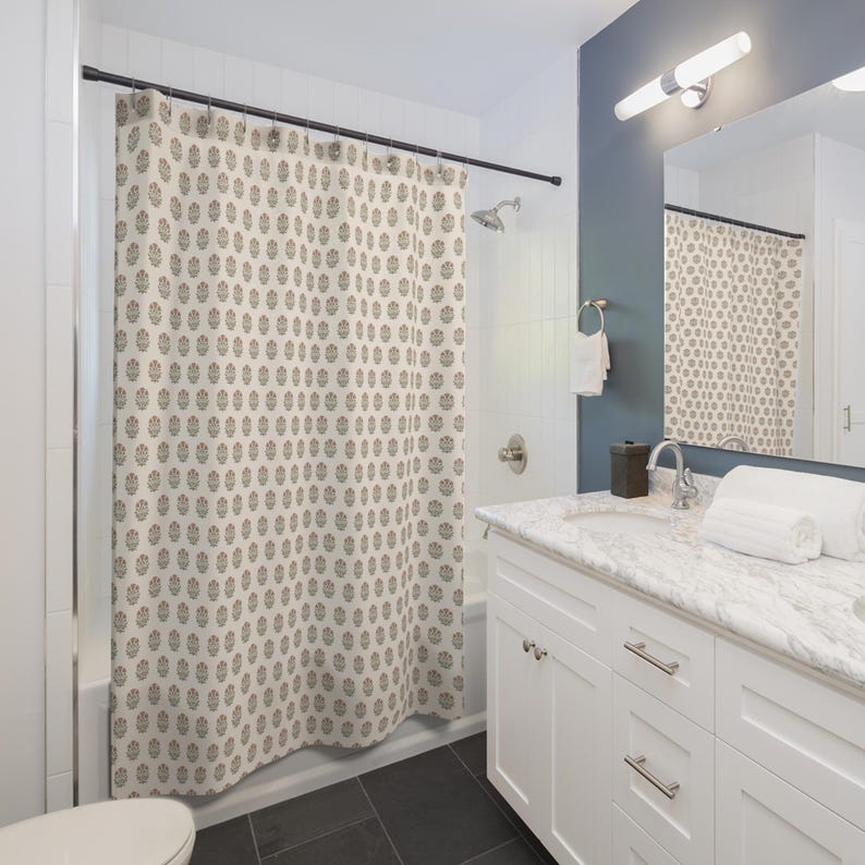 May include: A beige shower curtain with a repeating floral pattern in brown and gray. The curtain hangs in a bathroom with white cabinetry, a marble countertop, and a dark gray floor. A mirror reflects the curtain.