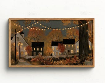 May include: A framed horizontal wall art print depicting a neighborhood scene at dusk with autumn foliage, several houses with glowing windows, a large tree trunk on the right, and a string of warm white fairy lights hanging across the dark sky.