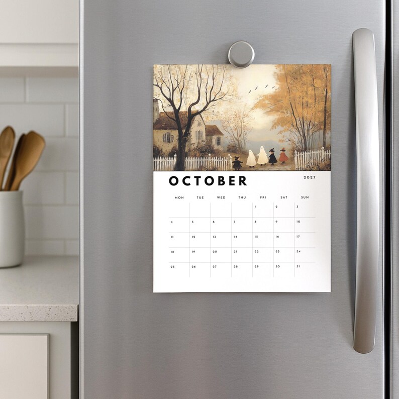 May include: A magnetic wall calendar for October 2027 featuring an illustration of a house, trees, and figures in costumes. The calendar has a white background with black text and a grid for dates. It is attached to a stainless steel surface.