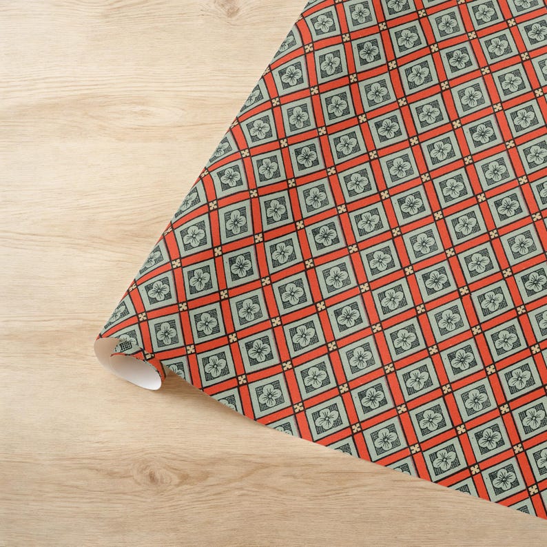 May include: A roll of wrapping paper featuring a repeating geometric grid pattern. The design consists of light green squares, each containing a small four-petaled flower, separated by bold orange bands and small black cross accents.