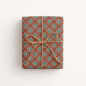 May include: A rectangular gift wrapped in paper featuring a repeating geometric pattern of orange diamonds and light blue squares, each containing a small four-petaled flower motif. The package is tied with a thin, natural brown jute twine bow.