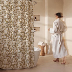 May include: Mustard-colored shower curtain with a white floral pattern. The curtain is hanging in a bathroom with a white bathtub and a wooden stool. A person wearing a white robe is in the background.
