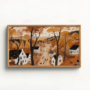 May include: A framed art print depicts a quaint village scene in autumn. The artwork features white houses with black roofs lining a street filled with people and dogs. The trees are filled with orange and yellow leaves.