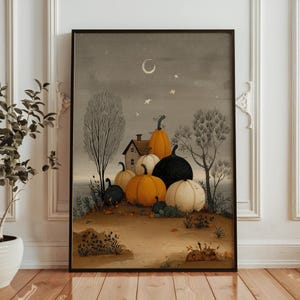 May include: Framed art print depicting an autumnal scene. The image shows a group of pumpkins in shades of orange, black, and white, gathered near a small house. The background features a night sky with a crescent moon and stars.