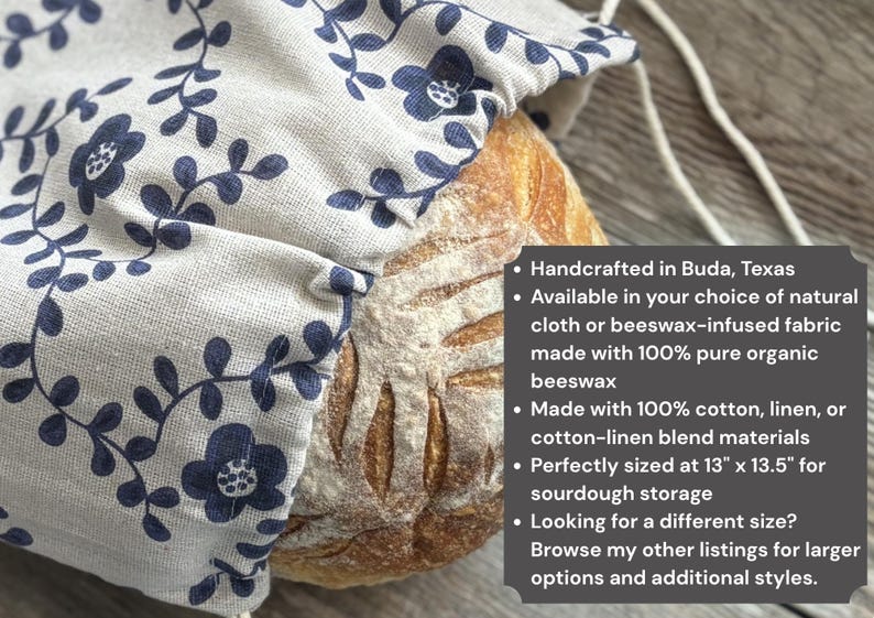 May include: A beige fabric bread bag with a dark blue floral vine pattern containing a round loaf of sourdough bread. A dark gray text box lists product details including dimensions of 13 inches by 13.5 inches and material options.