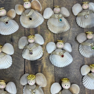May include: A collection of angel ornaments crafted from white ribbed seashells. Each angel features a small wooden bead head with painted facial details, a gold-tone halo, a gold ribbon collar, and a single dangling gemstone charm in various colors.