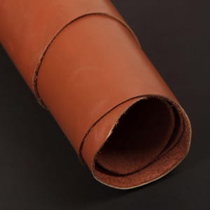 May include: A roll of brown leather, rolled up tightly. The leather is smooth and has a natural, rustic look.