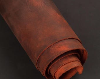 May include: Rolled-up sheet of distressed brown leather. The leather has a rich, reddish-brown color with visible grain and texture. The edges of the roll reveal the layers of the material, showcasing its thickness and flexibility. The background is a solid black.