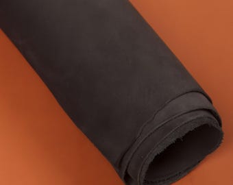 May include: A rolled-up piece of dark gray leather against an orange background. The leather appears to be thick and has a slightly textured surface. The edges of the roll are visible, showing the thickness of the material.
