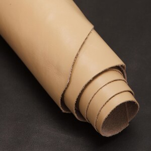 Puede incluir: Un rollo de cuero beige claro, enrollado apretadamente. El cuero es liso y parece ser de alta calidad.