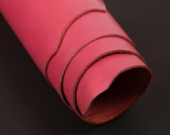 May include: Rolled sheet of vibrant pink leather, showcasing the smooth surface and the natural, textured edges. The leather is tightly rolled, revealing the layers and the rich, reddish-brown underside. The background is a solid, dark gray.